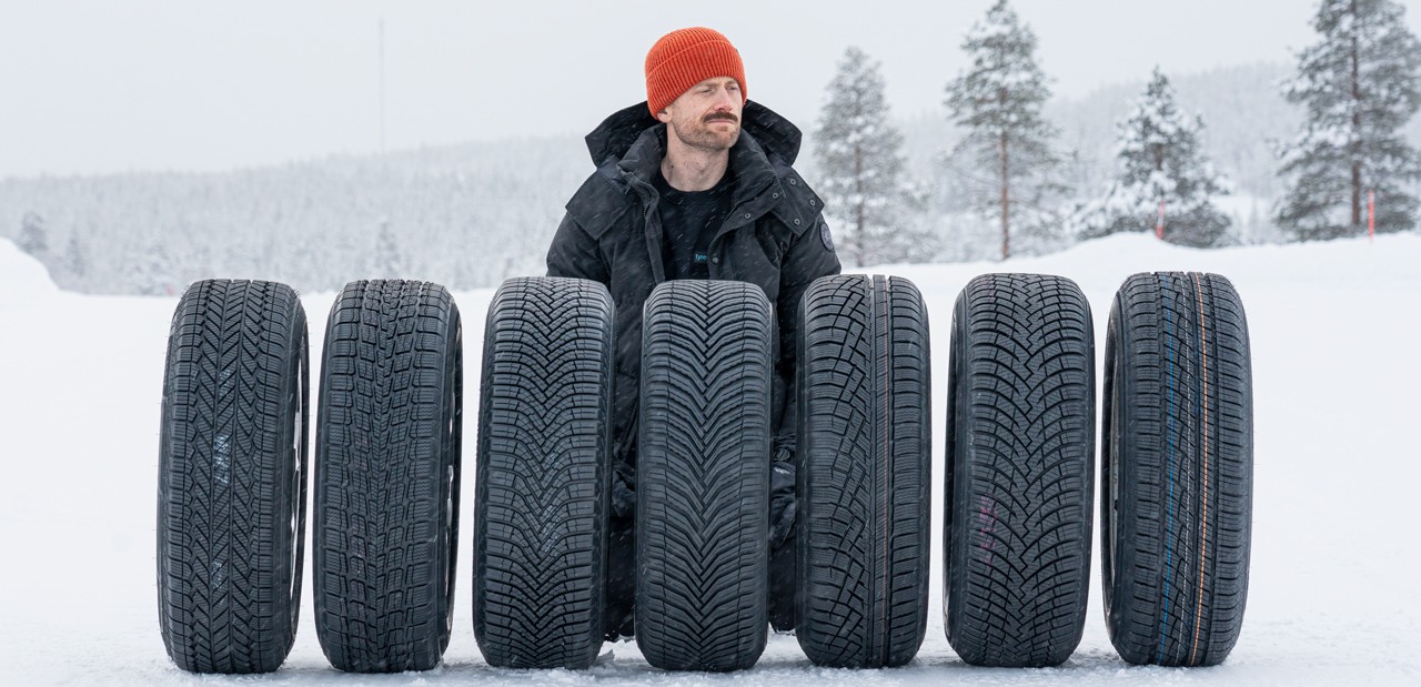 Jonathan Benson sobre la nieve detrás de una fila de neumáticos todo clima en una prueba de Tyre Reviews