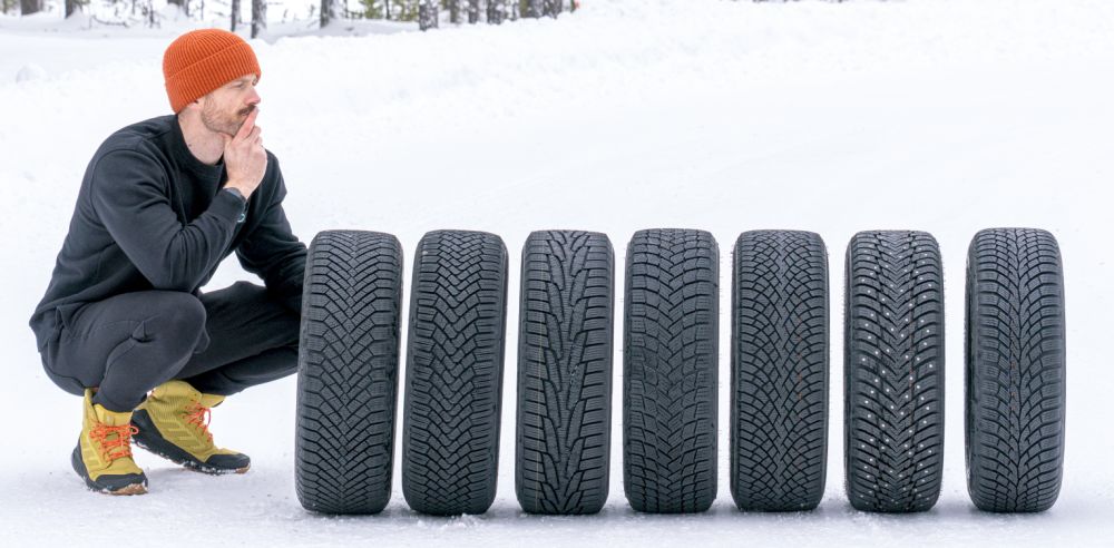 Jonathan Benson agachado junto a una fila de neumáticos de invierno sobre la nieve
