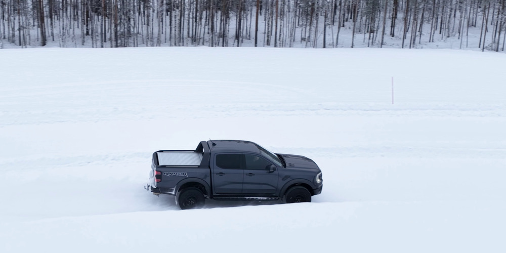 Ford Ranger Raptor gris circulando por un circuito de pruebas nevado junto a un bosque